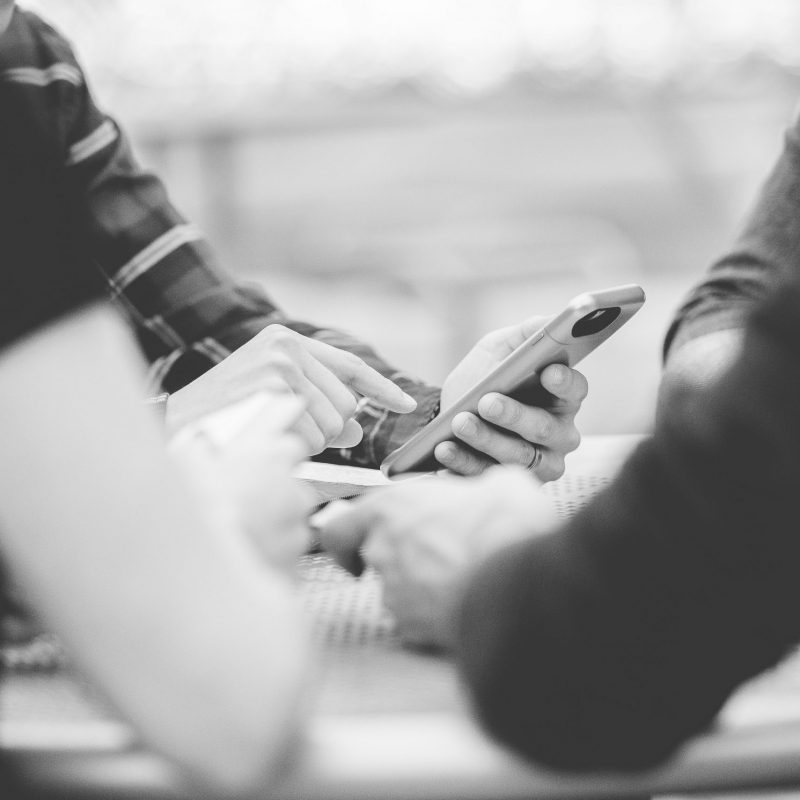 A closeup shot of people using their smartphone with a blurred background in black and white